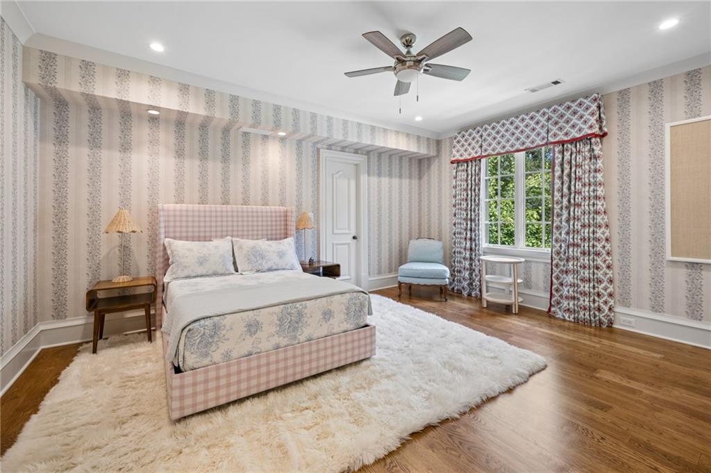 Bedroom with a pink checked bed, striped wallpaper, and a large curtained window.