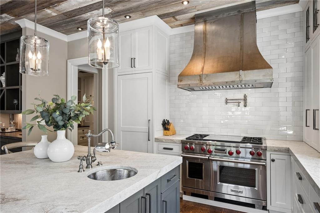 Kitchen with a gray island, stainless range, copper hood, and rustic wood ceiling.