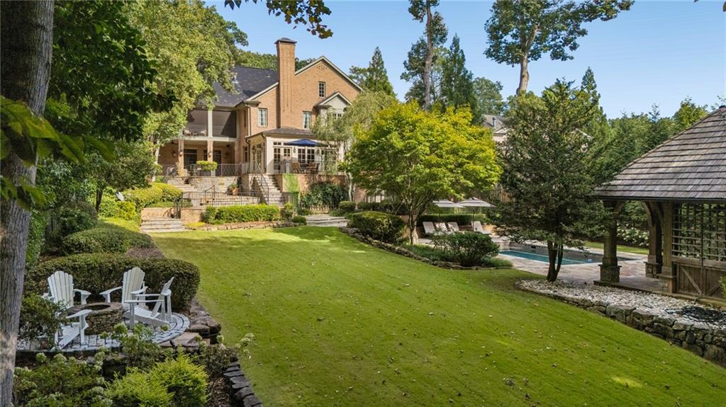 Landscaped backyard with a brick house, broad lawn, swimming pool, pavilion, and outdoor seating.