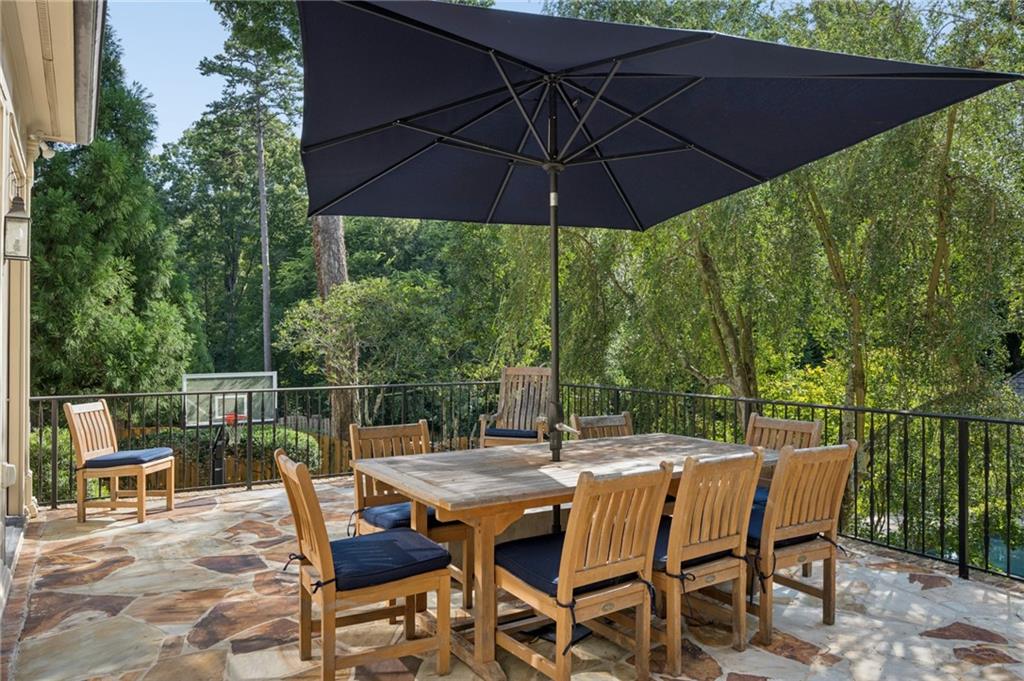 Stone patio dining area with wooden furniture and a large umbrella, overlooking dense greenery.