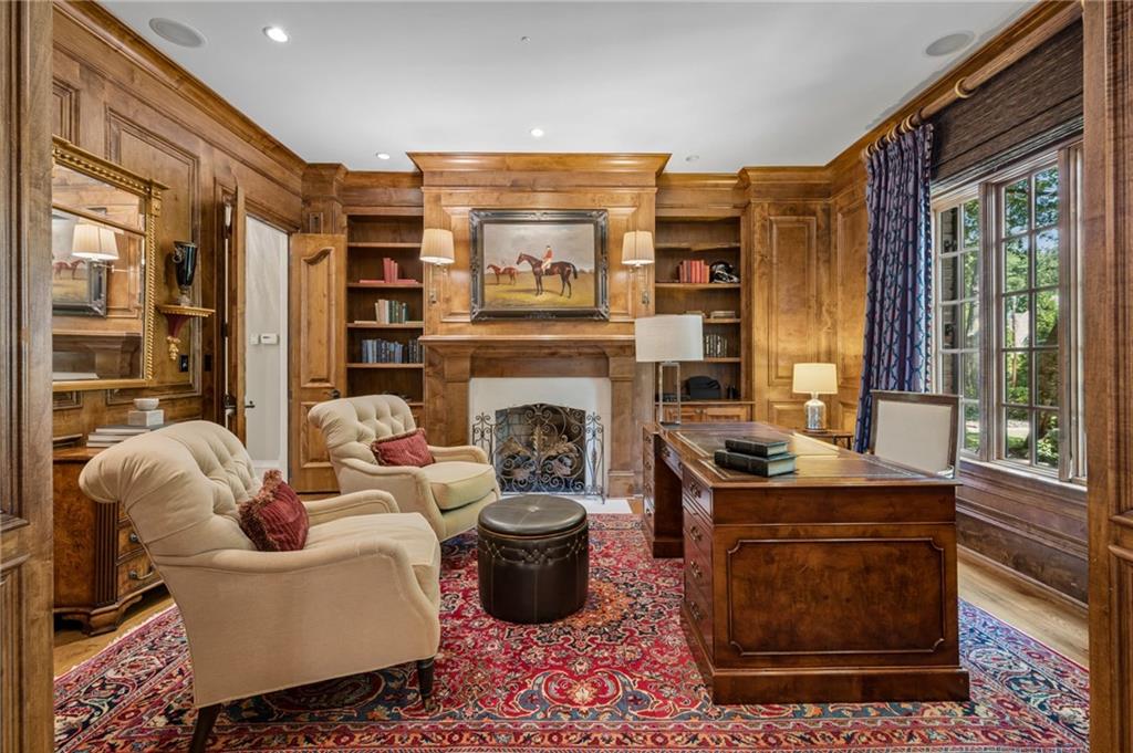 Wood-paneled study with built-in bookcases, fireplace, desk, and large curtained windows.
