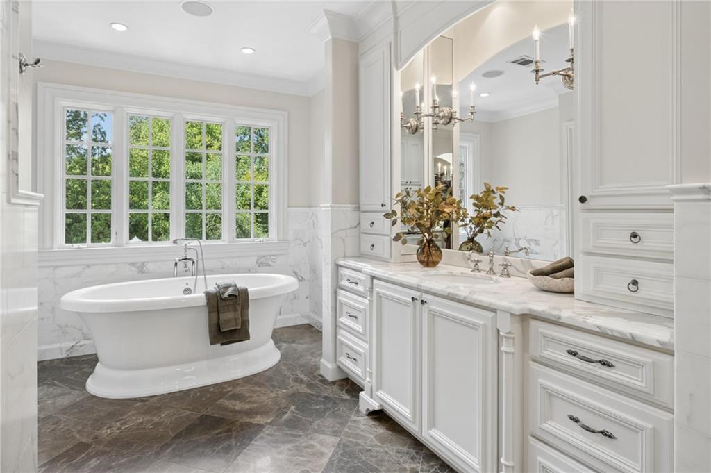 Bright bathroom with a freestanding soaking tub, tree-view windows, and a marble-topped white vanity.