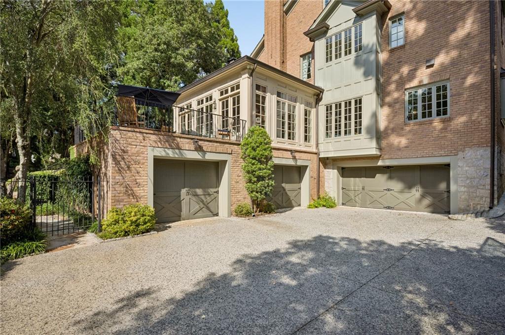 Brick house with three garage doors beneath a raised terrace, viewed across a gravel driveway.