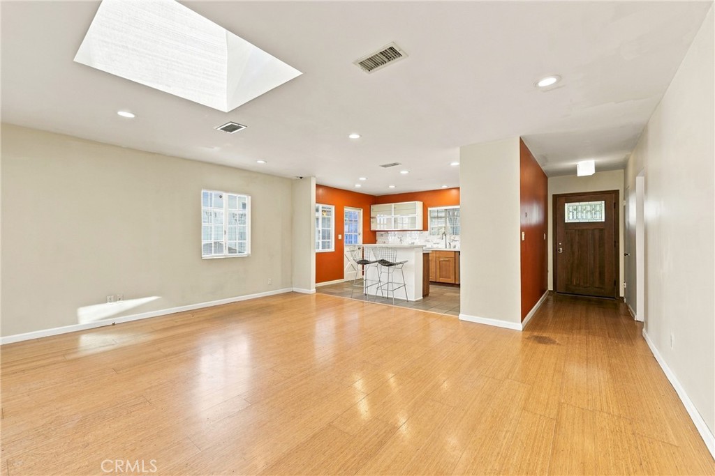 Open living area with hardwood floors, a large skylight, and an orange-accented kitchen.
