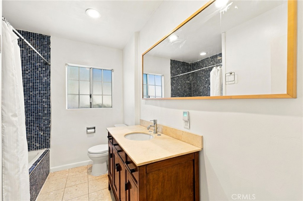 Bathroom with dark blue tiled tub surround, wood vanity, and large framed mirror.