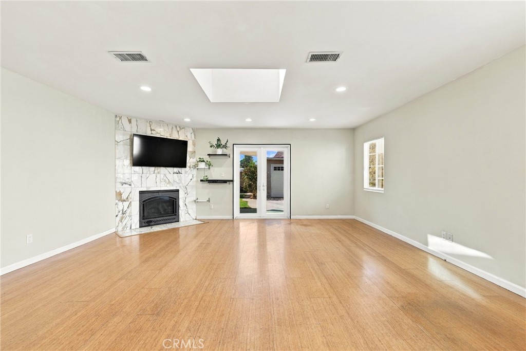 Empty living room with a marble fireplace surround, mounted television, and hardwood floor.