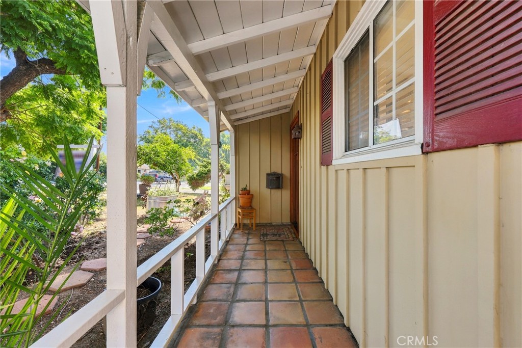 Covered front porch with terracotta tile flooring and red shutters.