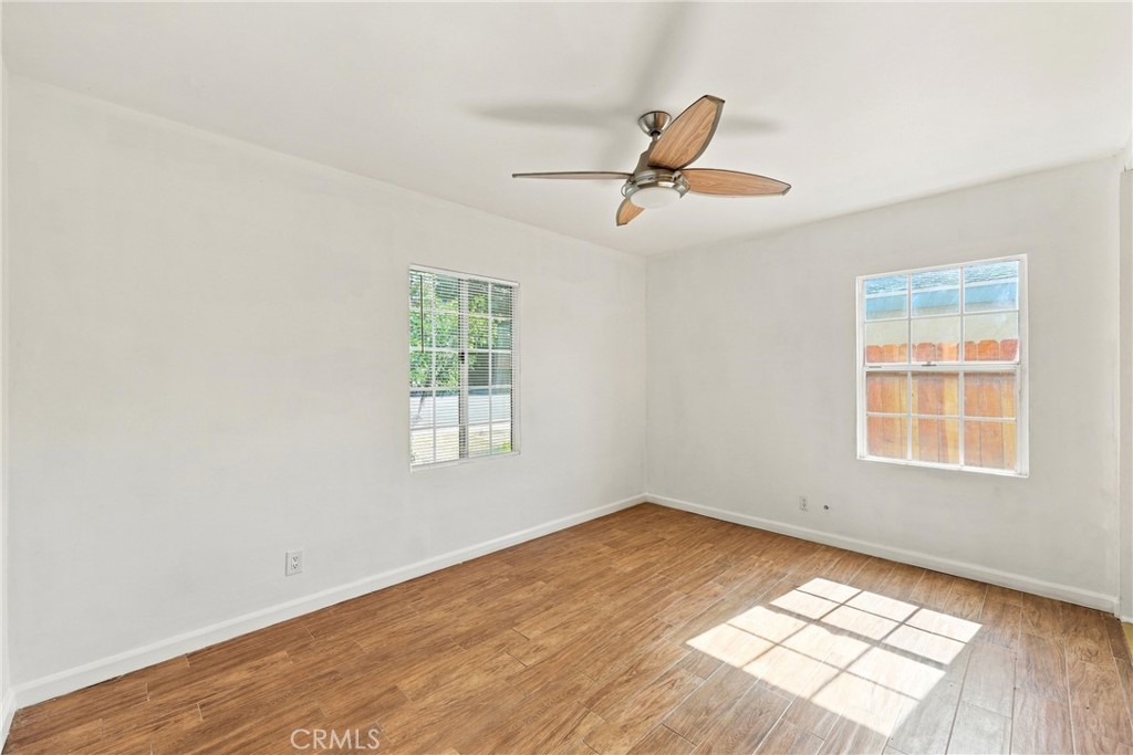 Empty room with wood flooring, two windows, and a ceiling fan.