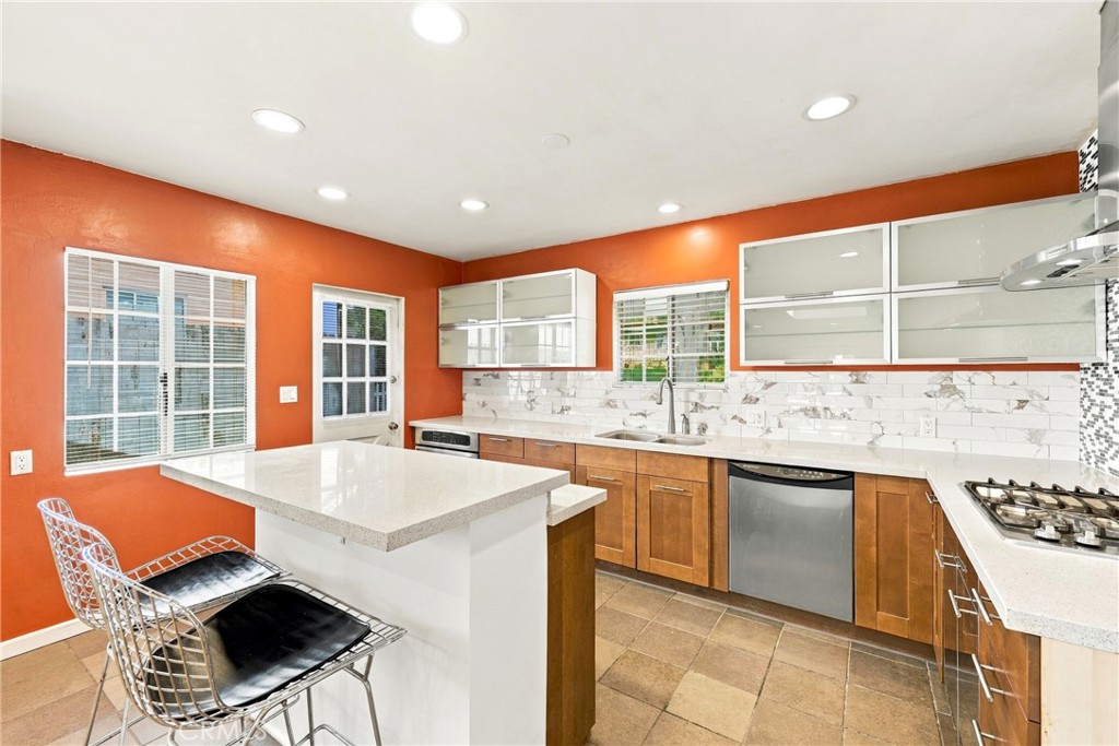 Kitchen with a white island, warm wood cabinets, and a marble-pattern backsplash against orange walls.