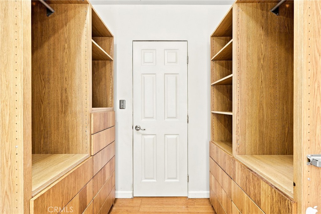 Walk-in closet with built-in oak shelving and drawers on both sides of a white door.