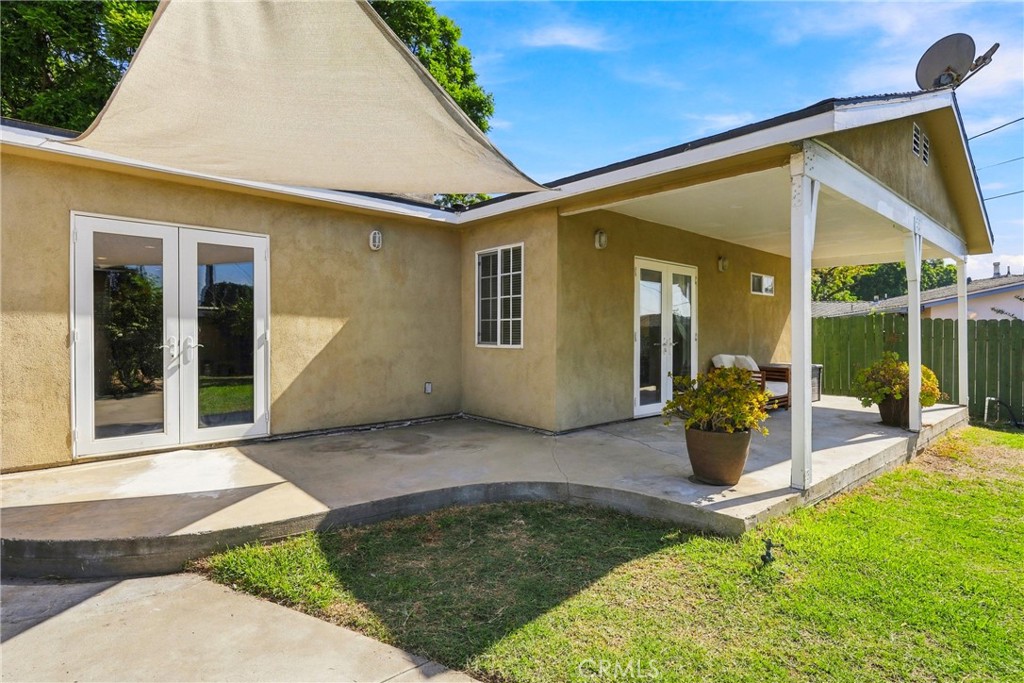 Rear patio with a covered porch, French doors, a shade sail, and lawn.