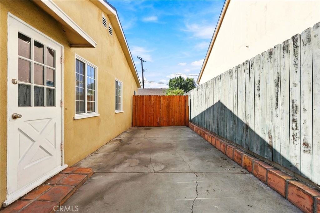 Paved side yard between the house and a weathered fence, ending at a wooden gate.