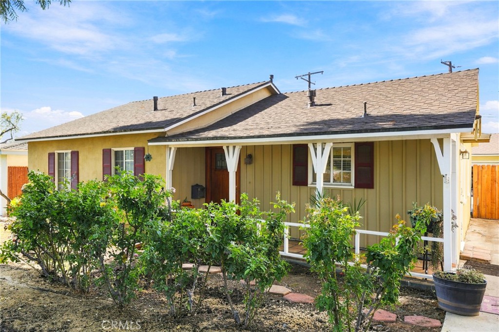 Single-story yellow house with a long covered porch, white supports, and leafy front shrubs.