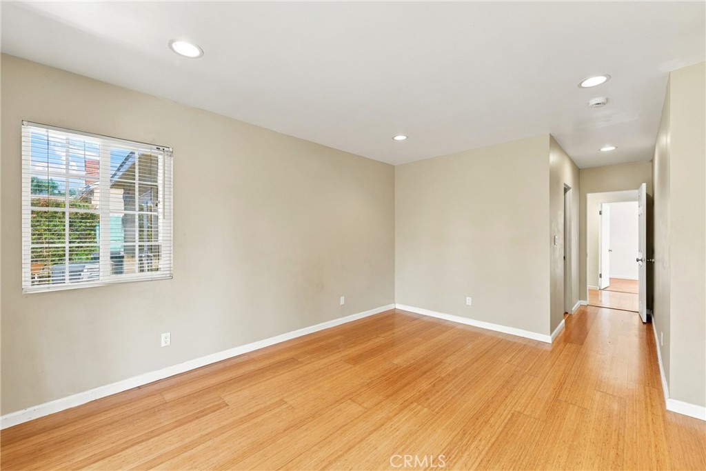 Empty room with hardwood floors, recessed lights, and a window beside a hallway.