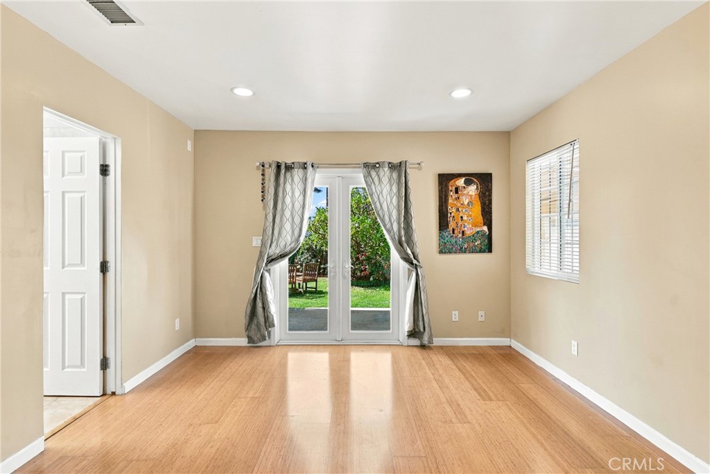 Empty room with wood flooring, gray curtains, and glass doors opening to a garden.
