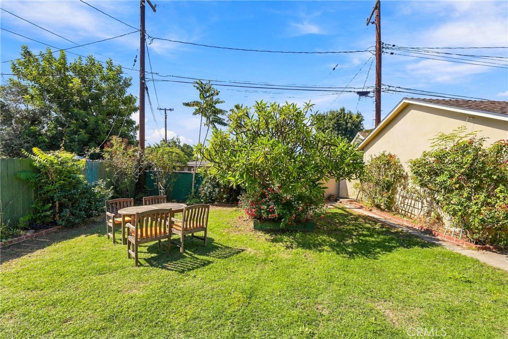 Backyard with a lawn, patio dining set, flowering shrubs, and a large shade tree.
