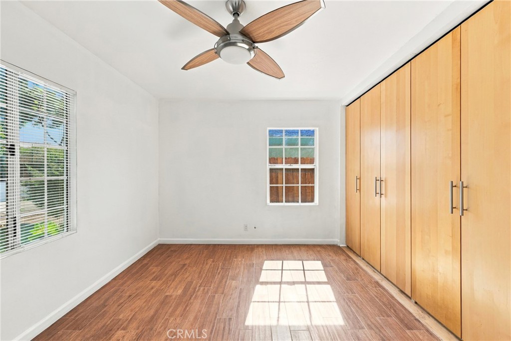 Empty bedroom with floor-to-ceiling wood closets, wood-look flooring, and a ceiling fan.