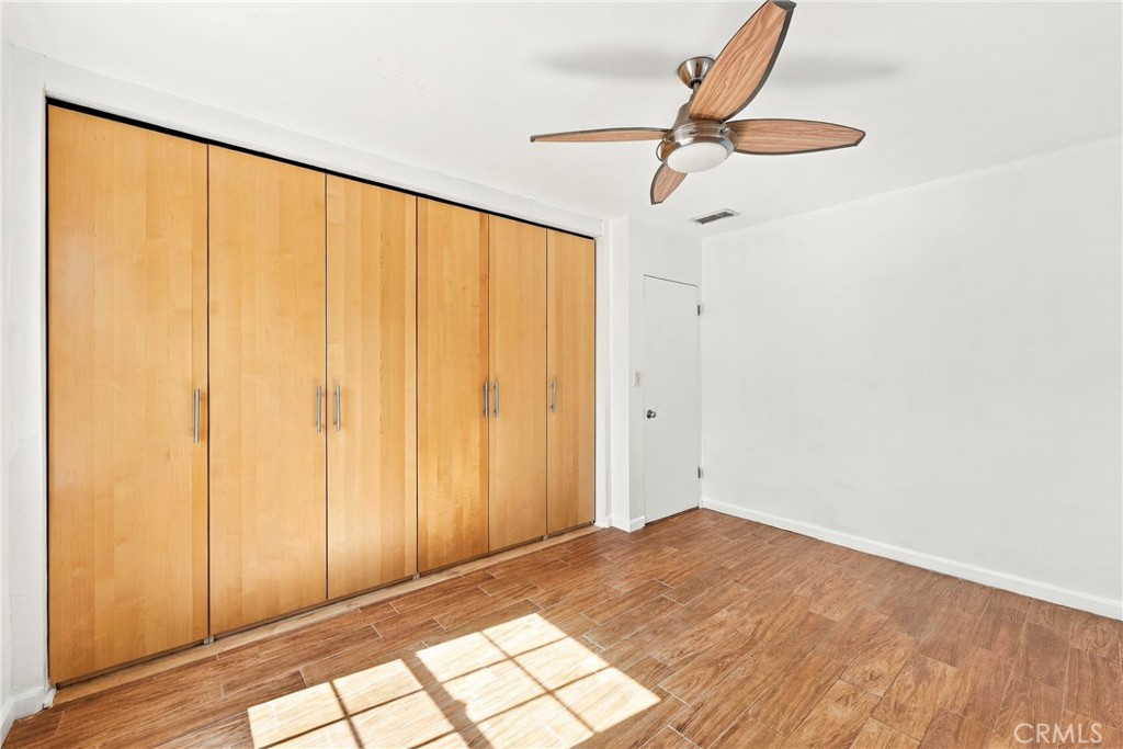 Vacant bedroom with wall-length wood closets, wood-look flooring, and a ceiling fan.