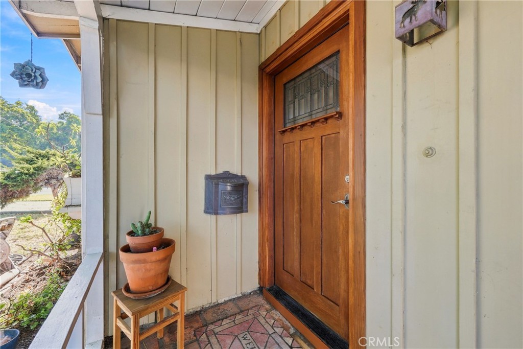 Covered front porch with a wood entry door, stained-glass panel, and potted plants.