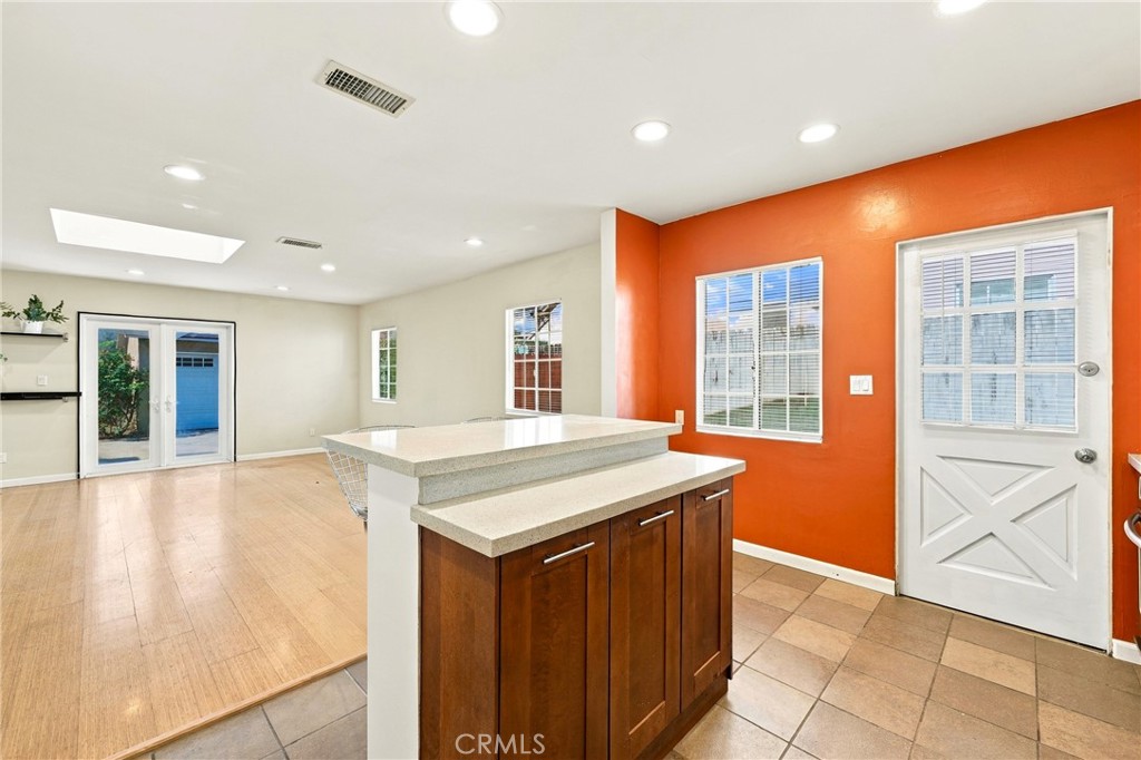 Kitchen island with dark wood cabinets beside an open living area and orange accent wall.