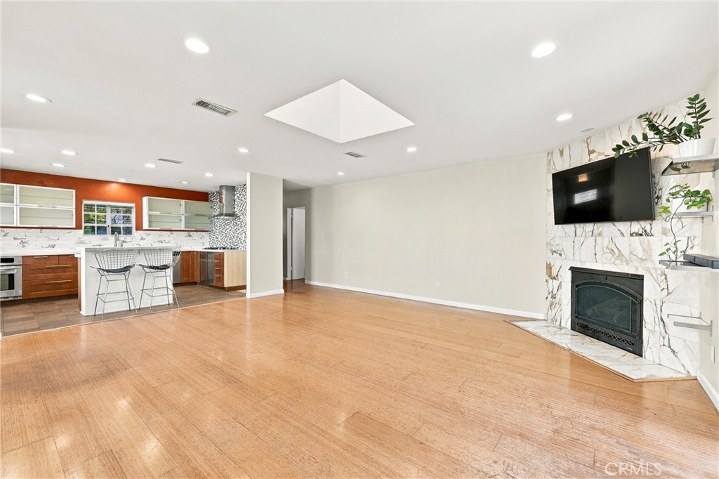 Open living room with wood flooring, a marble fireplace, and adjoining kitchen.