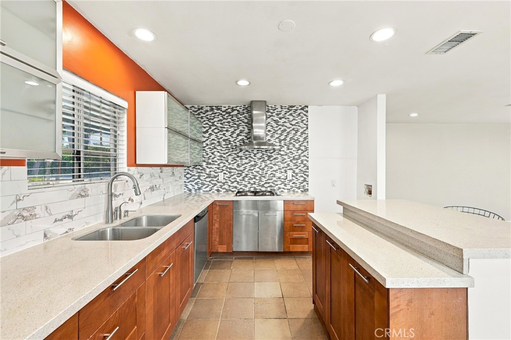 Kitchen with warm wood cabinetry, peninsula counter, mosaic backsplash, and stainless steel appliances.