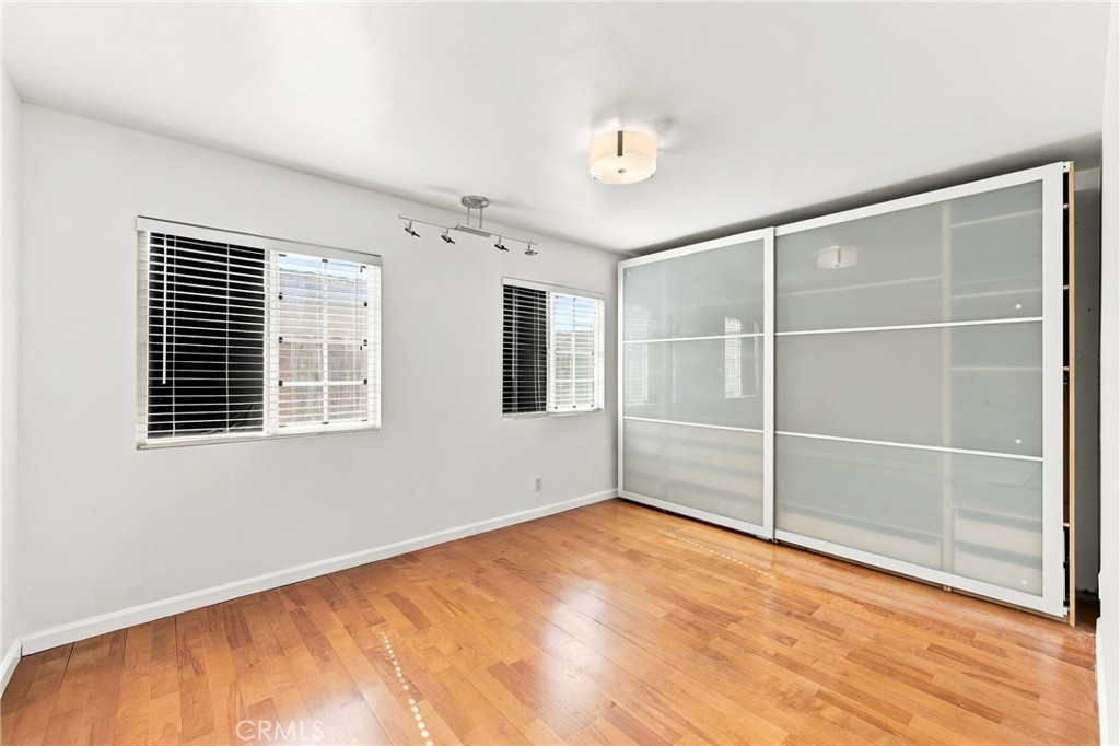 Empty bedroom with wood flooring, two windows, and large sliding closet doors.