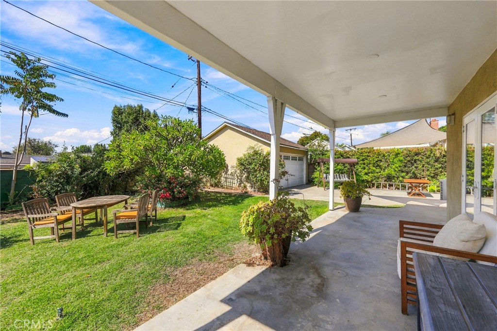 Covered patio overlooking a grassy backyard with outdoor dining furniture and a detached garage.