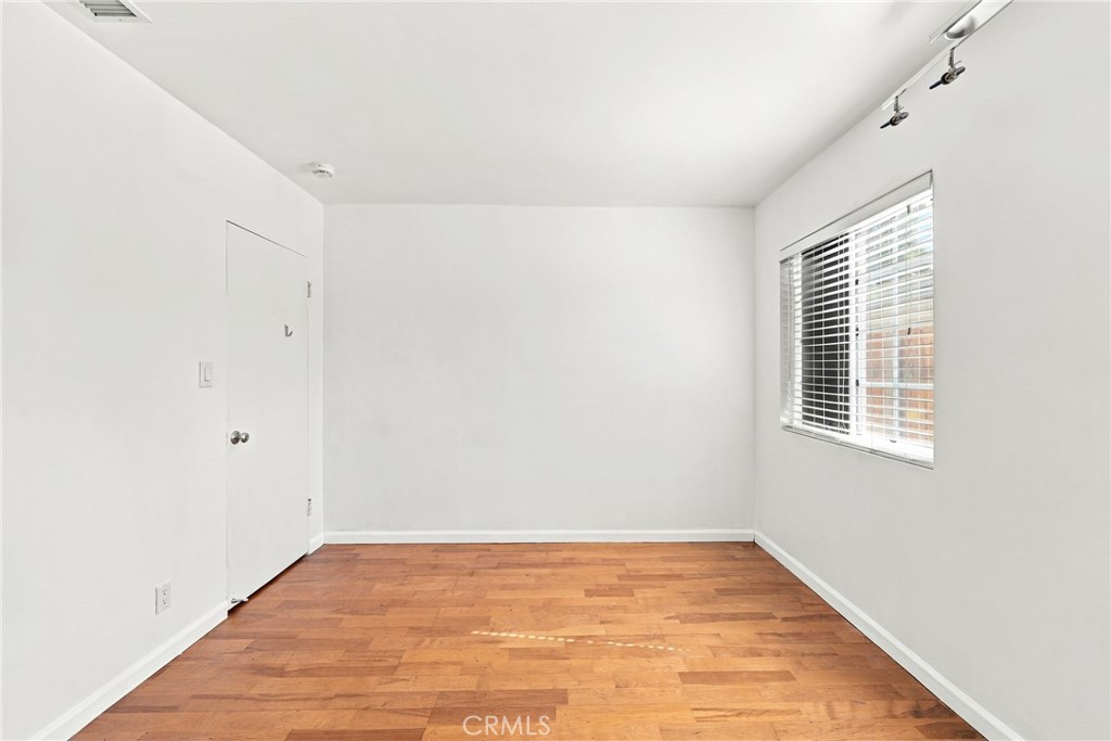 Empty room with warm wood flooring, white walls, and a window with blinds.