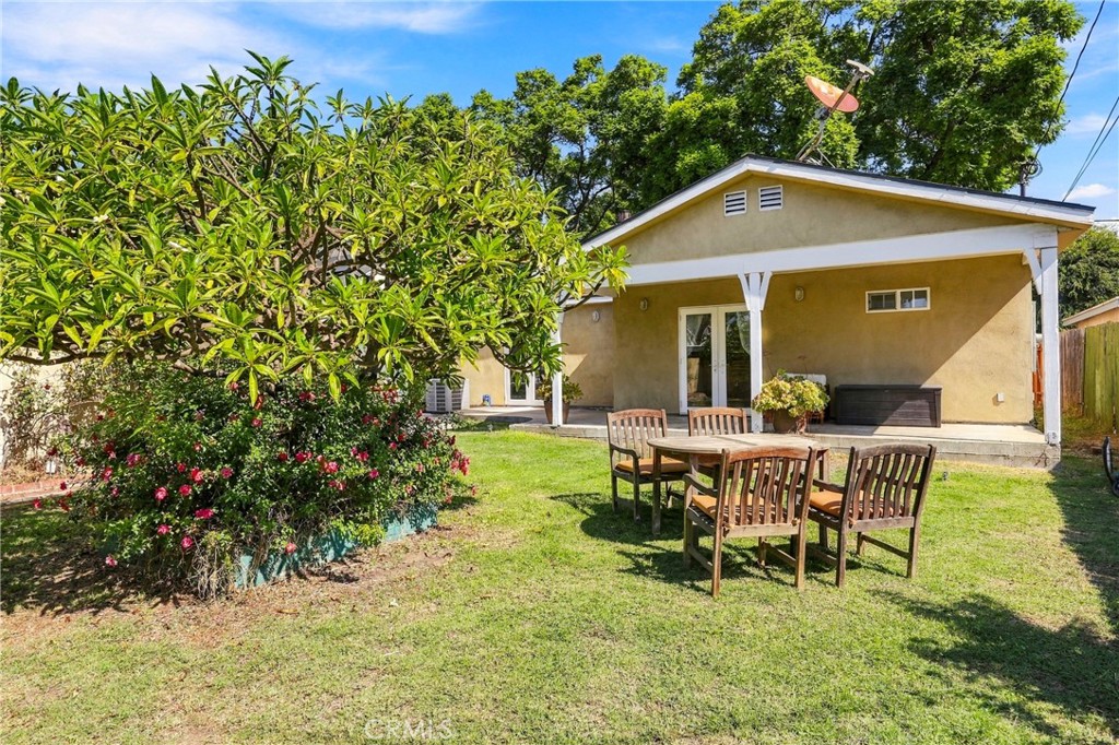 Rear of a tan home with a covered patio, lawn, and outdoor dining set.