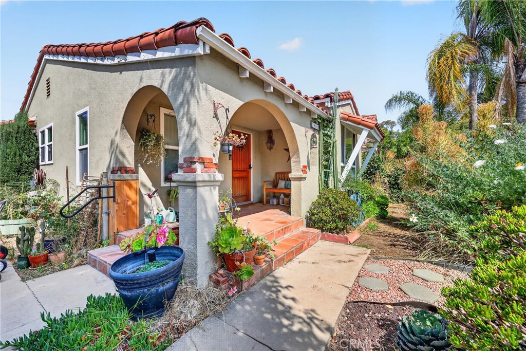 Stucco home with a terracotta tile roof, arched porch, red front door, and lush garden.