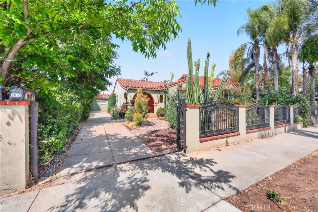 Spanish-style home behind a black metal gate, with a red tile roof and tall cacti.
