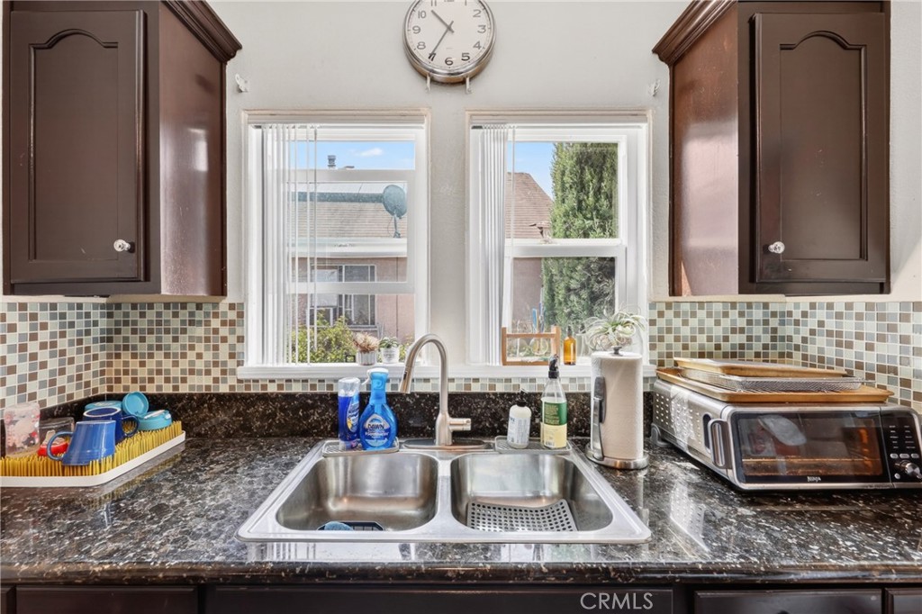Kitchen with dark wood cabinets, mosaic tile backsplash, and a double-basin sink beneath two windows.