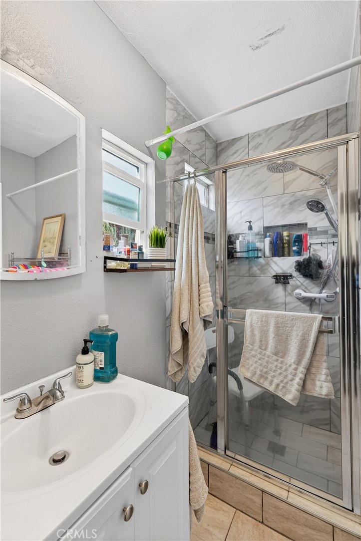 Bathroom with a white vanity and a tiled glass shower with chrome fixtures and beige towels.