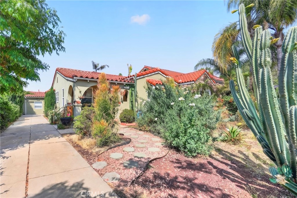 Single-story stucco home with a red tile roof, driveway, and large cactus in the front garden.
