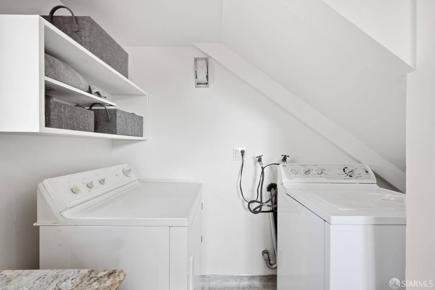 Laundry room with a washer and dryer beneath a sloped ceiling and open storage shelves.