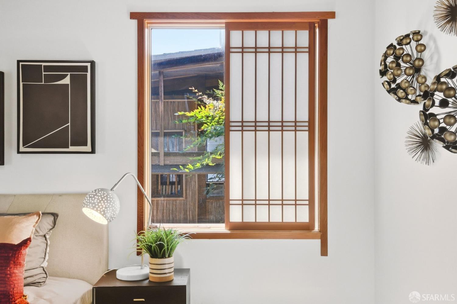 Bedroom with a wood-framed shoji-style window overlooking a leafy courtyard.