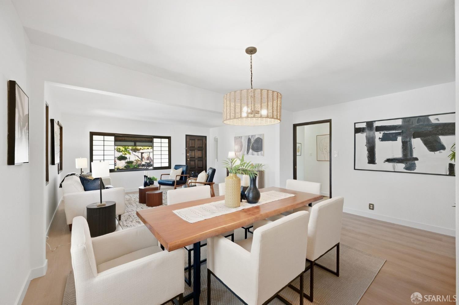Open-plan dining and living room with a wood table, white chairs, and woven pendant light.