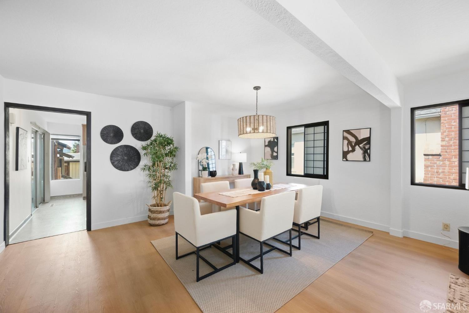 Dining room with a wood table, upholstered chairs, woven pendant light, and black-trimmed windows.