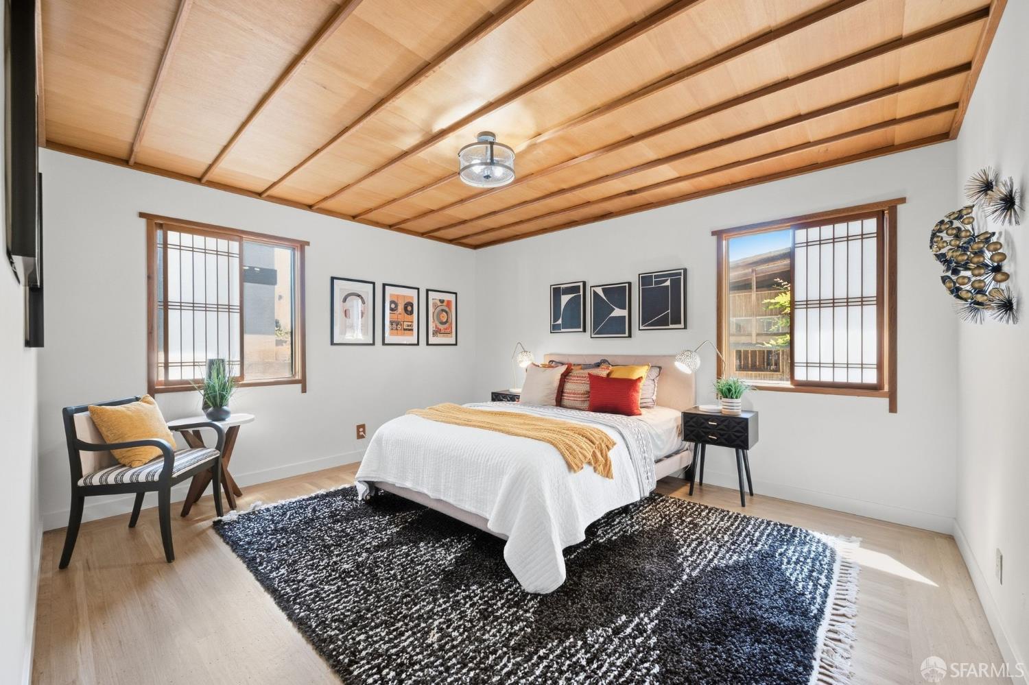 Furnished bedroom with a white bed, large black-and-white rug, and warm wood-beam ceiling.