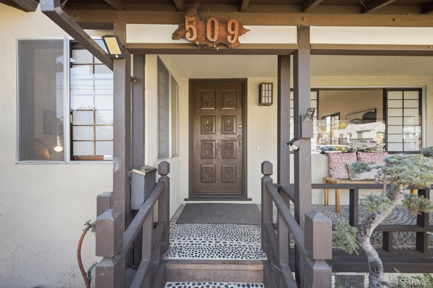 Home entrance with carved wooden door, covered porch, and pebble-mosaic walkway.
