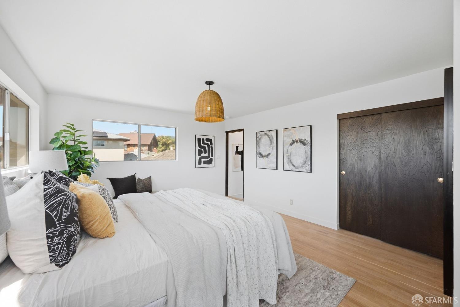 Bright staged bedroom with a white bed, woven pendant light, and dark wood closet doors.