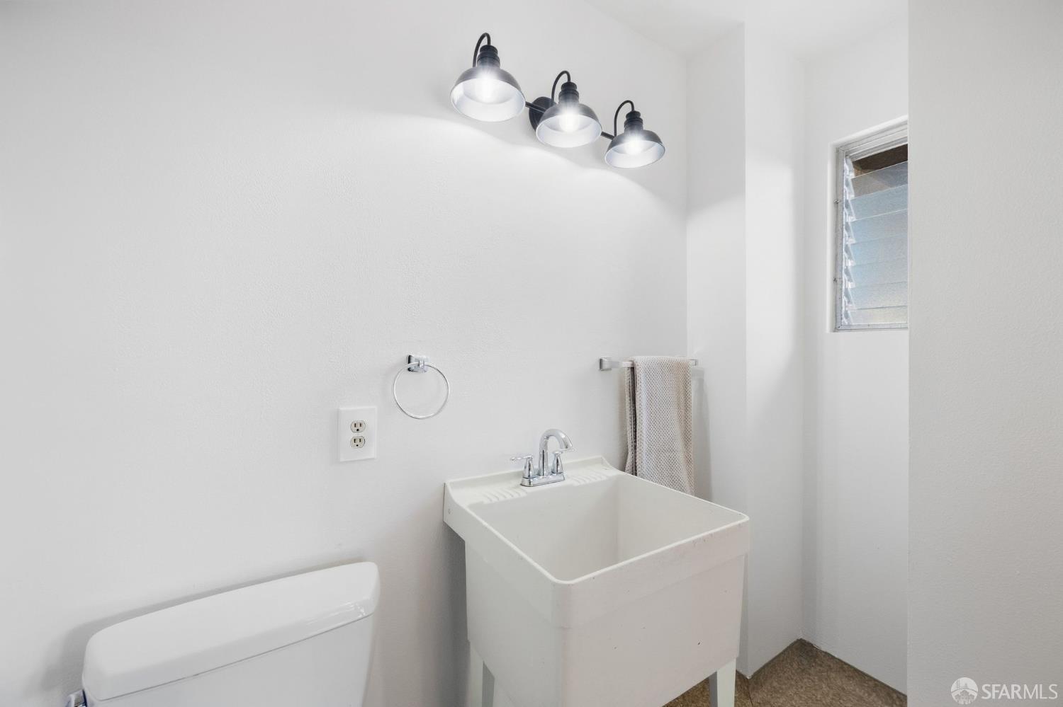 Bathroom with a deep white sink, chrome fixtures, and a louvered window.