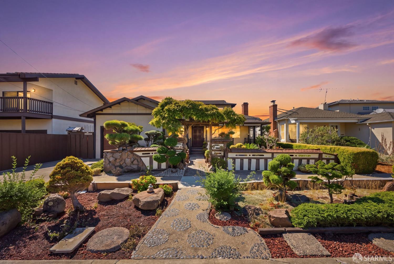Home with a sculpted garden and stone path beneath a purple-and-orange sunset.