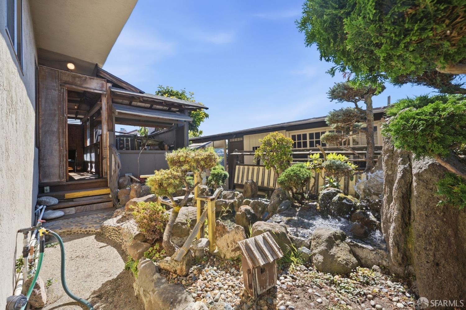 Landscaped courtyard with a rock-lined pond and waterfall beside a covered wooden entry.