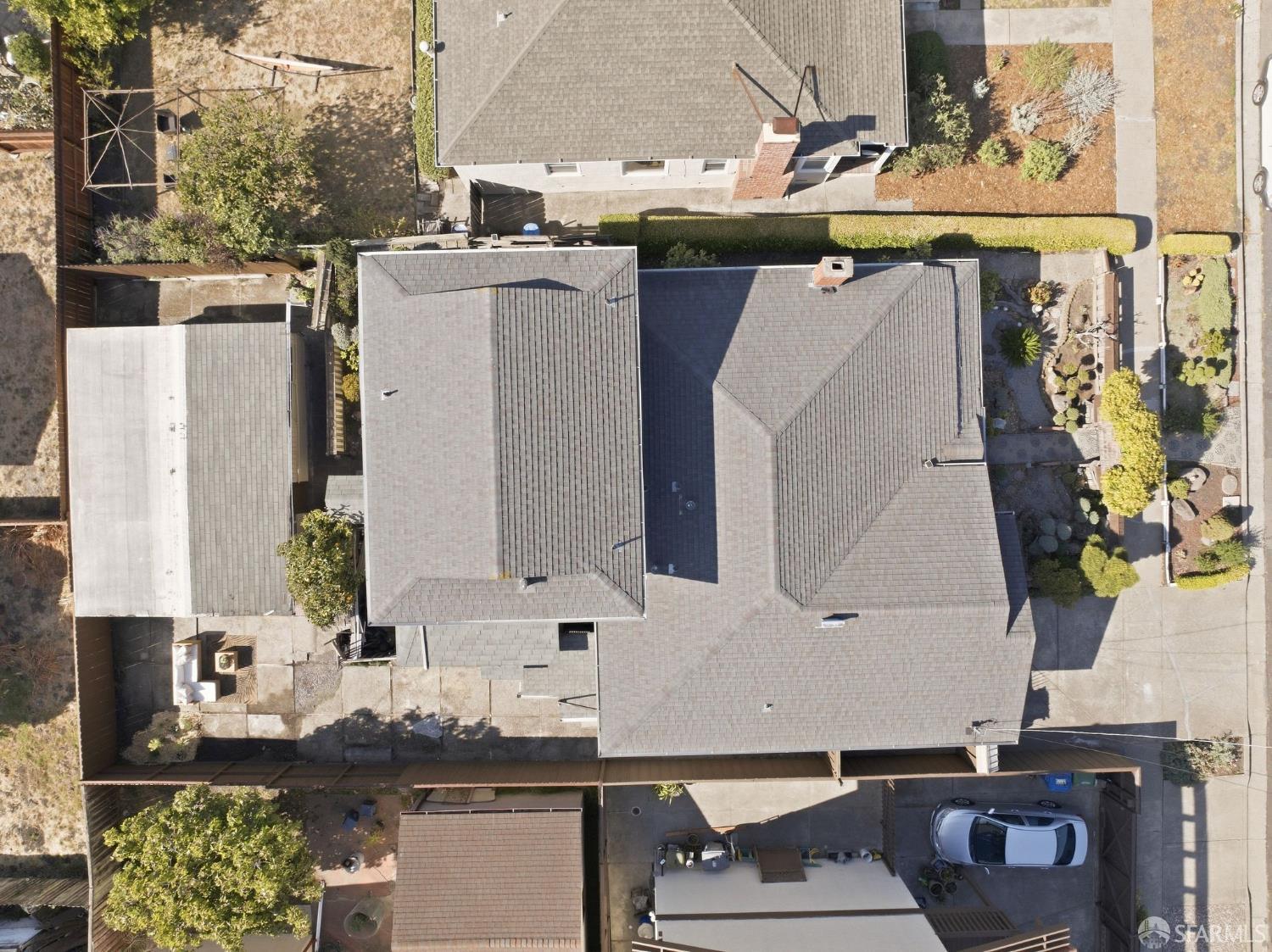 Aerial view of a home with a broad gray shingle roof, driveway, and landscaped side yard.