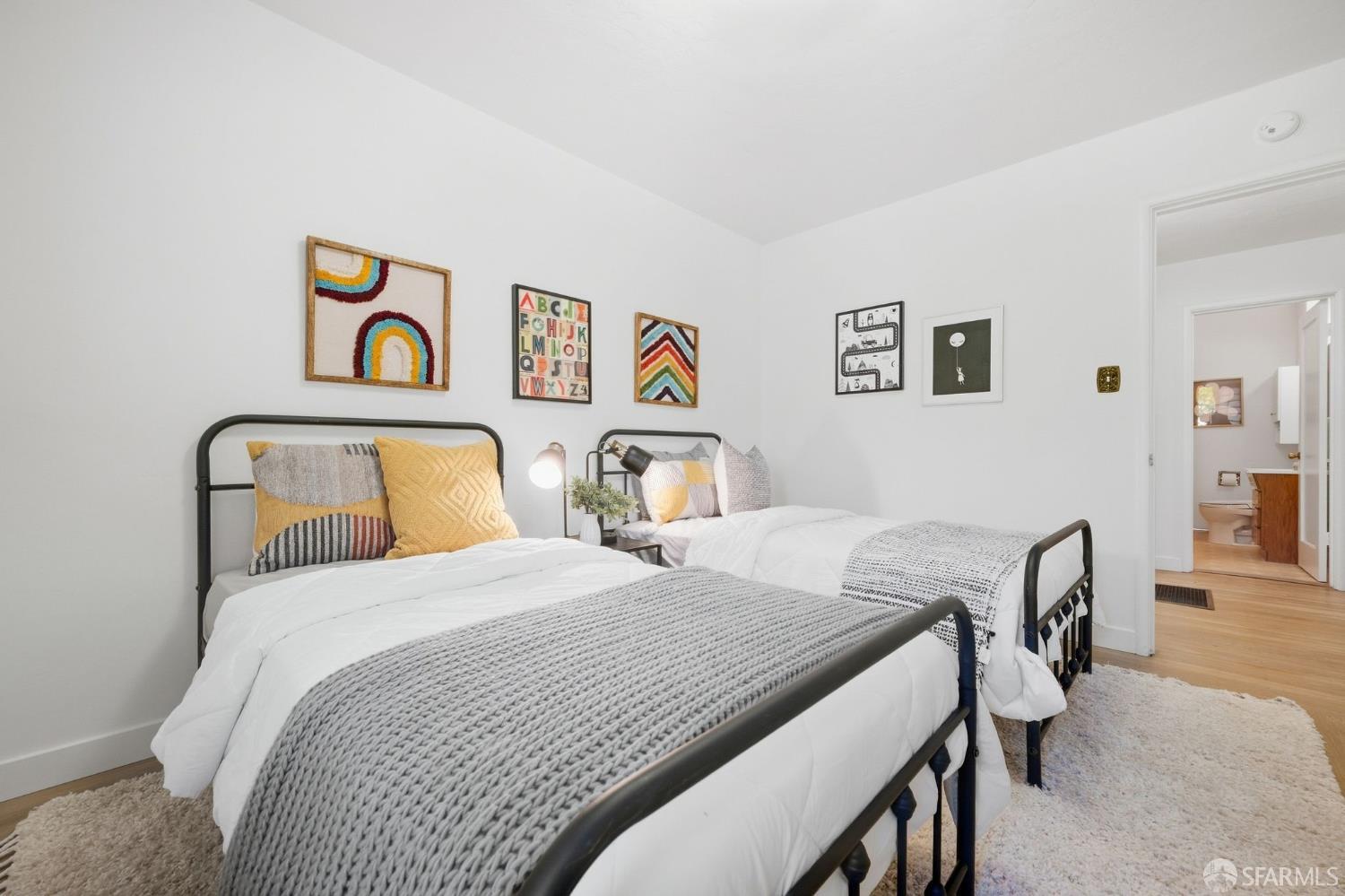 Bedroom with two black metal twin beds, gray knit blankets, colorful pillows, and framed wall art.