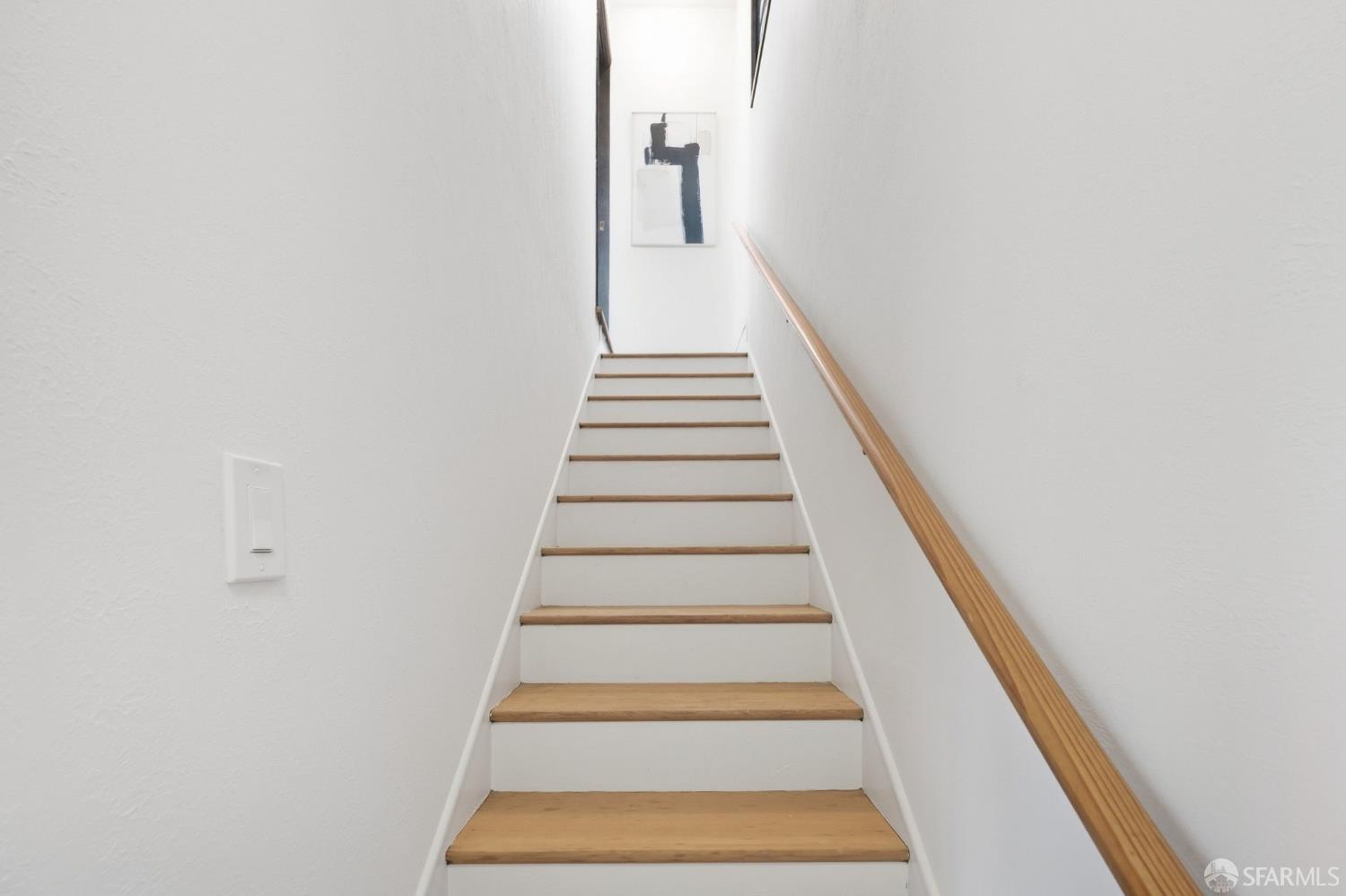 Narrow white staircase with natural wood treads and a wooden handrail.
