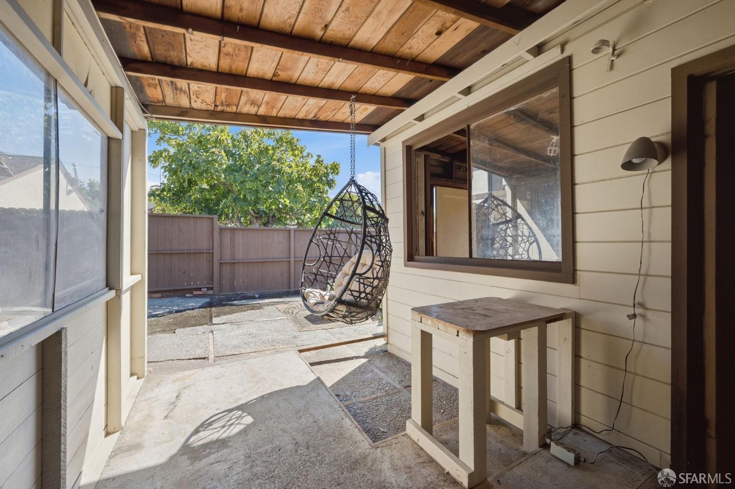 Covered backyard patio with a hanging egg chair, wood-plank ceiling, and fenced yard.