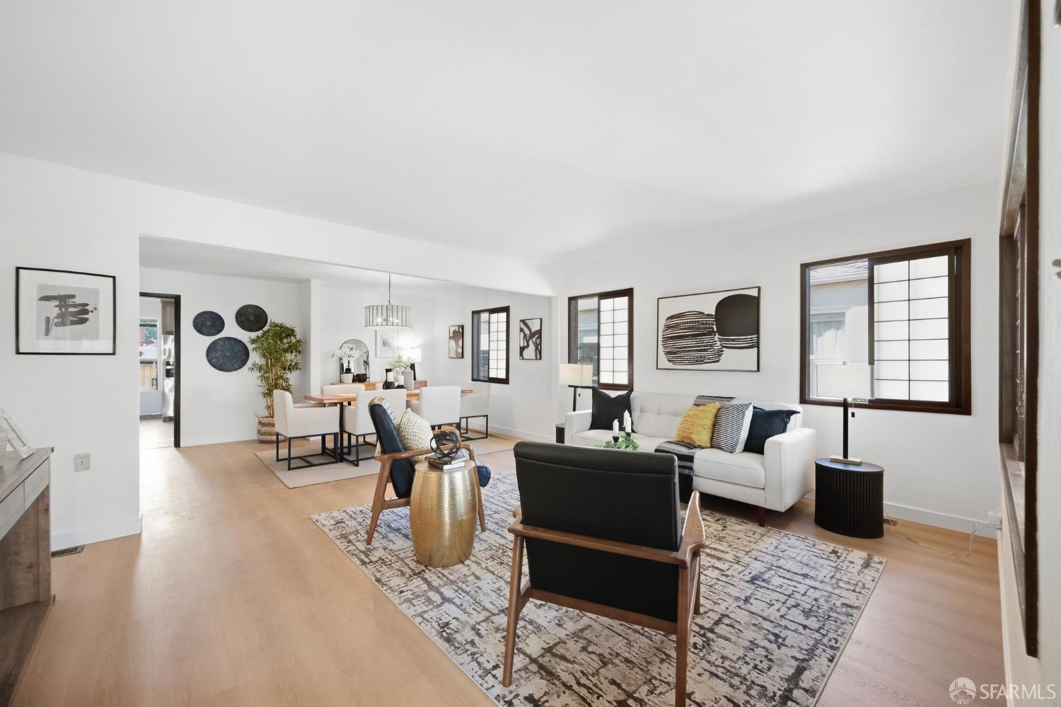 Staged living room with a white sofa, dark accent chairs, patterned rug, and adjoining dining area.